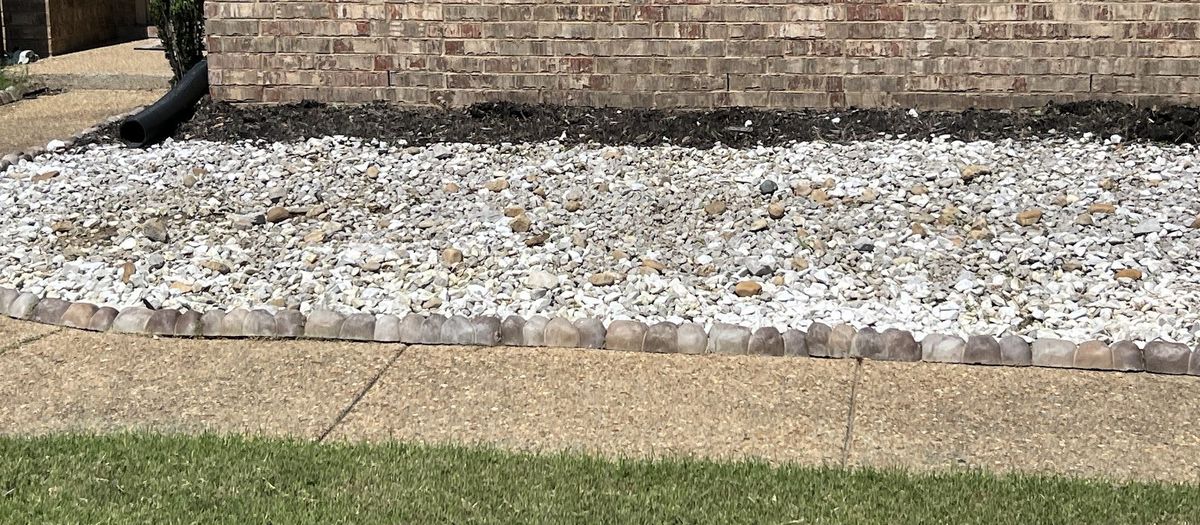 White landscape rock bed along a brick foundation with a stone edge beside the walk.